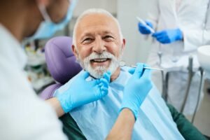رجل كبير في السن يبتسم أثناء فحص أسنانه في عيادة، مثال على زراعة الأسنان لكبار السن